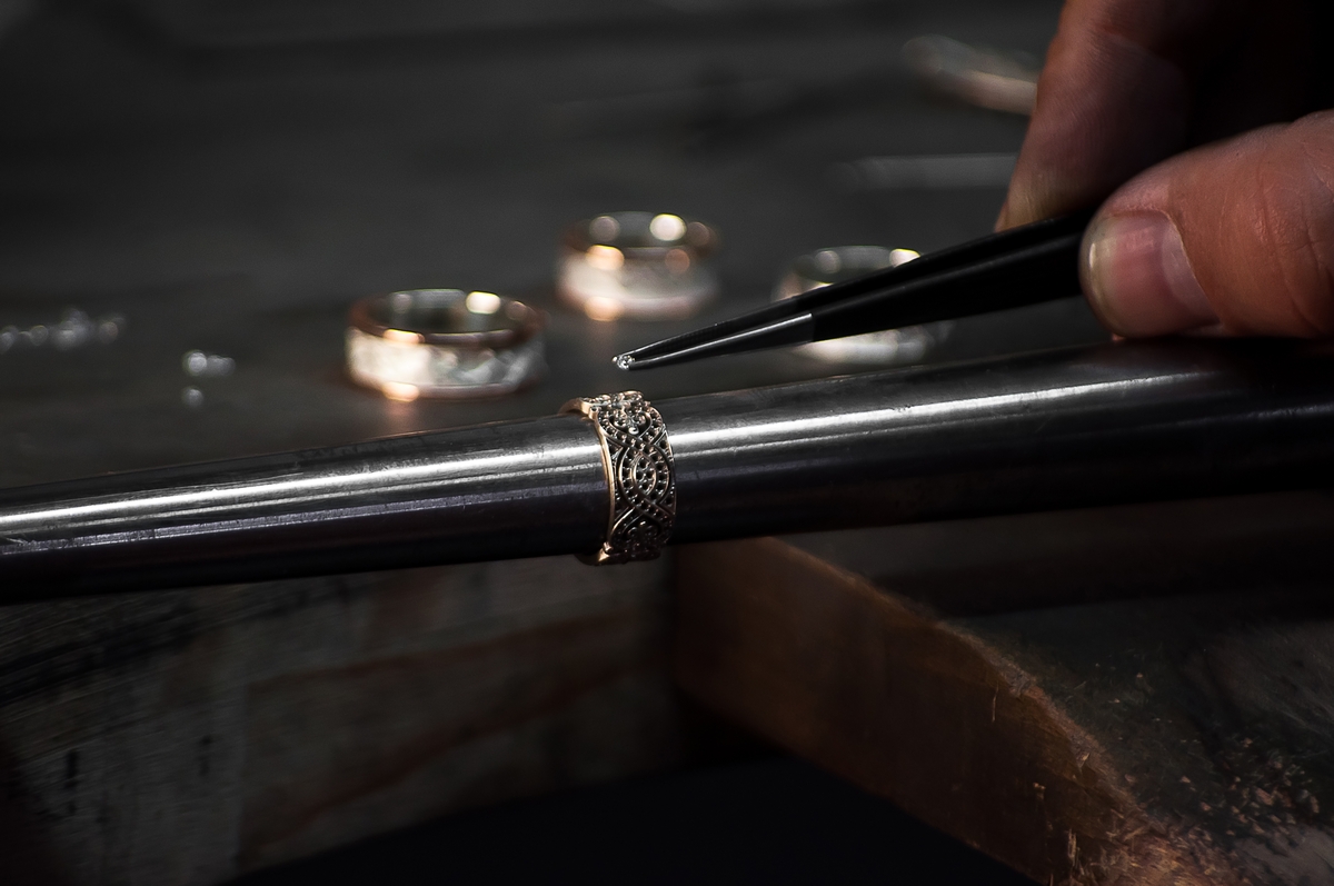 Close-up of hand of a goldsmith setting a precious stone with diamonds Ring repairing. Putting the diamond on the ring. Craft jewelery making with professional tools.